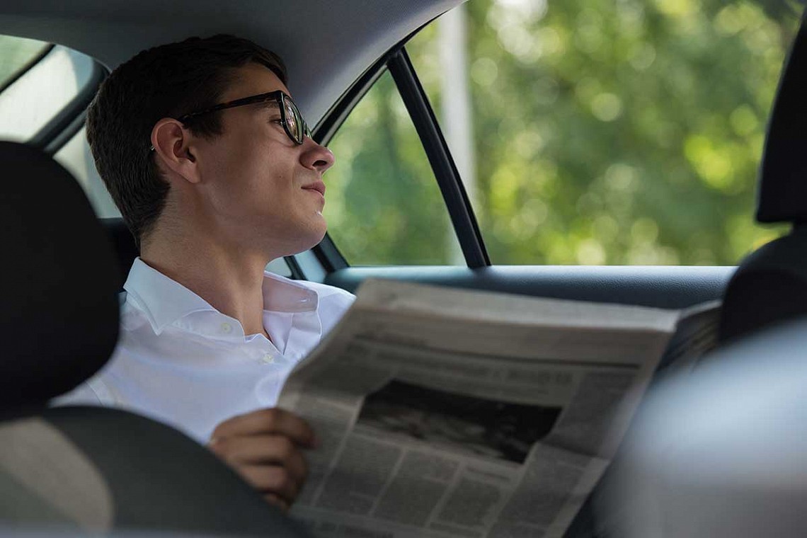 A man relaxing reading a newspaper in a car